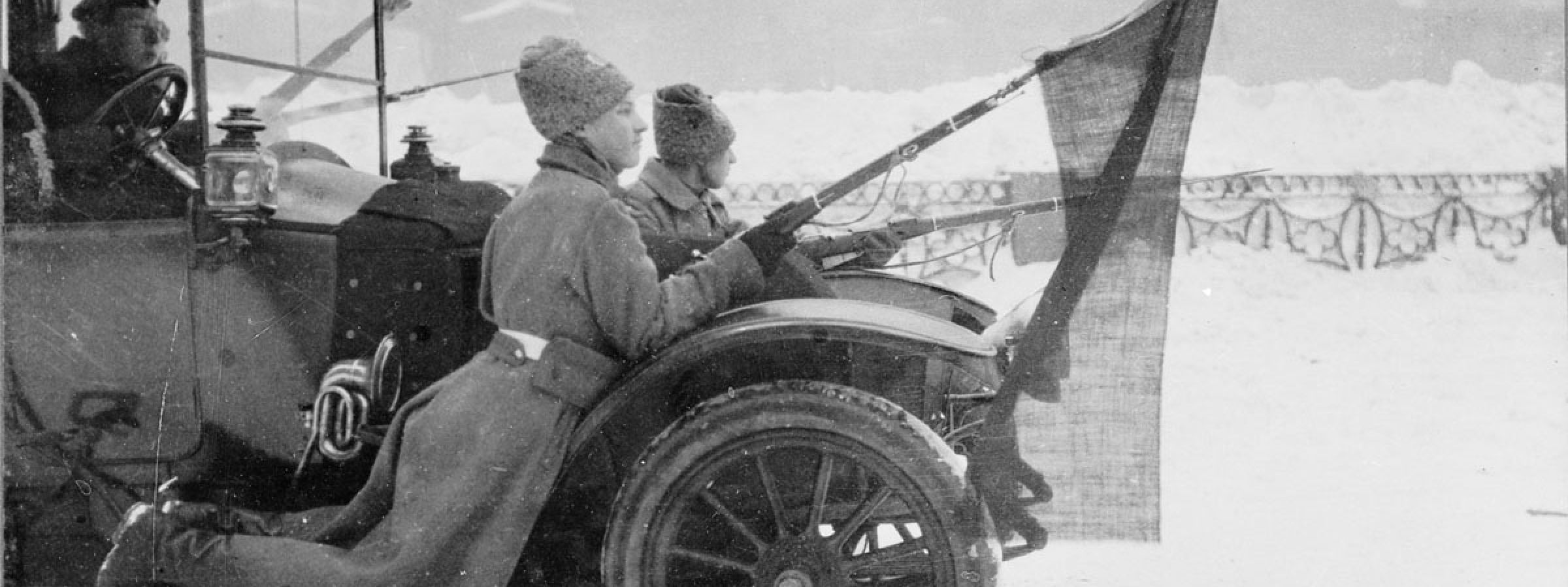 Two Russian soldiers, travelling via motor car through Petrograd, hold red flags affixed to their rifles during the revolution.